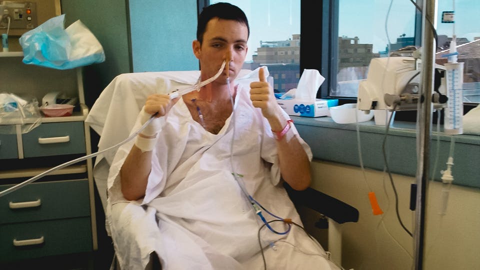 Dan Haslam, a supporter of medical marijuana, sits in a hospital bed giving the thumbs up