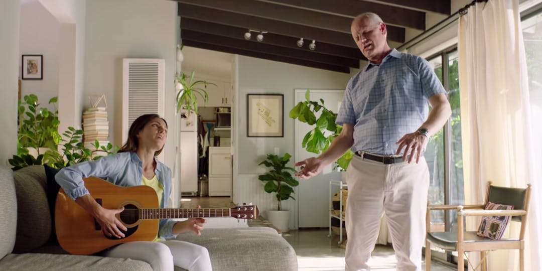 Woman playing guitar while high old man dances beside her