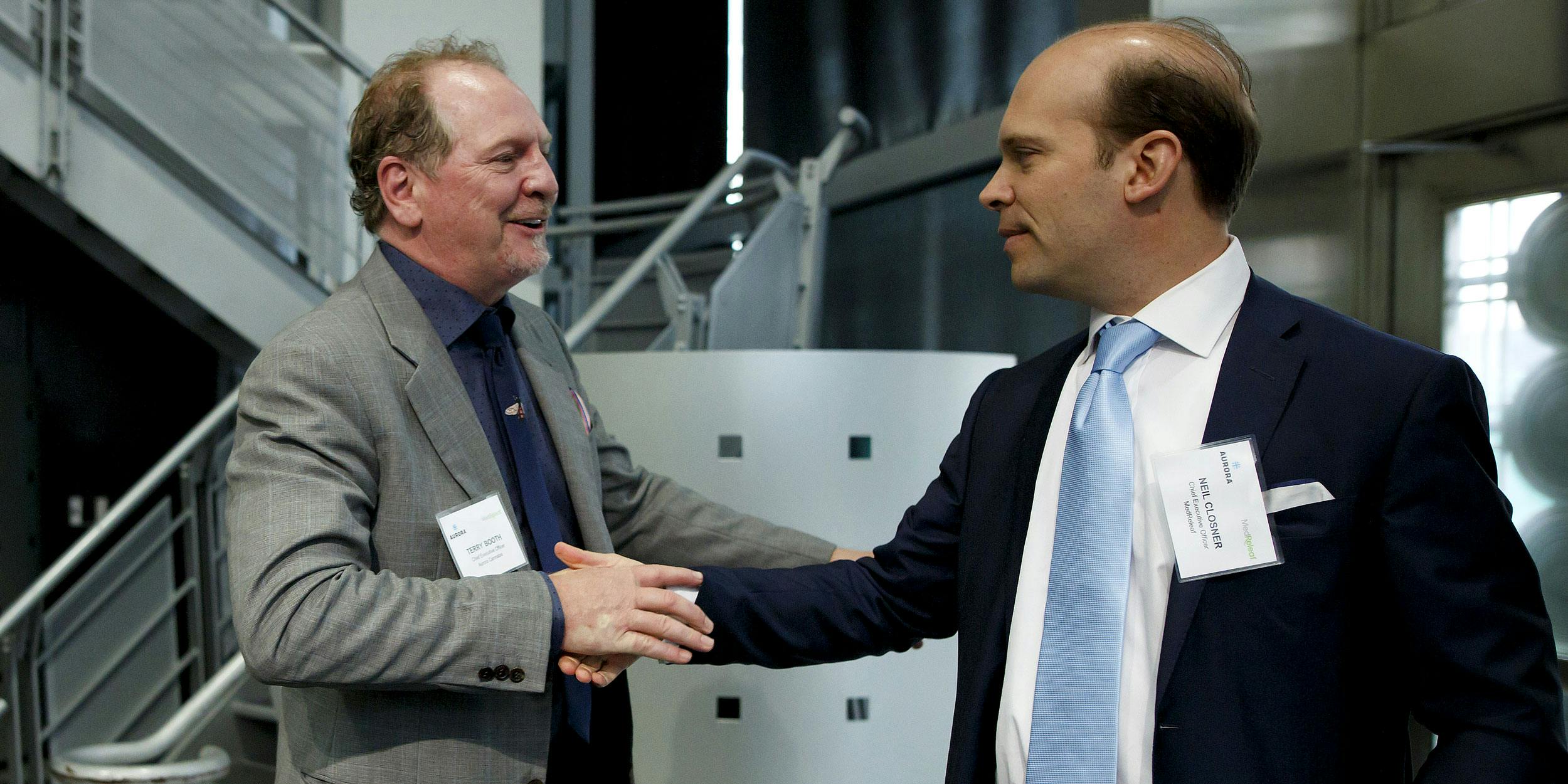 Terry Booth, chief executive officer of Aurora Cannabis Inc., left, shakes hands with Neil Closner, chief executive officer of MedReleaf Corp., during a news conference at the Toronto Stock Exchange