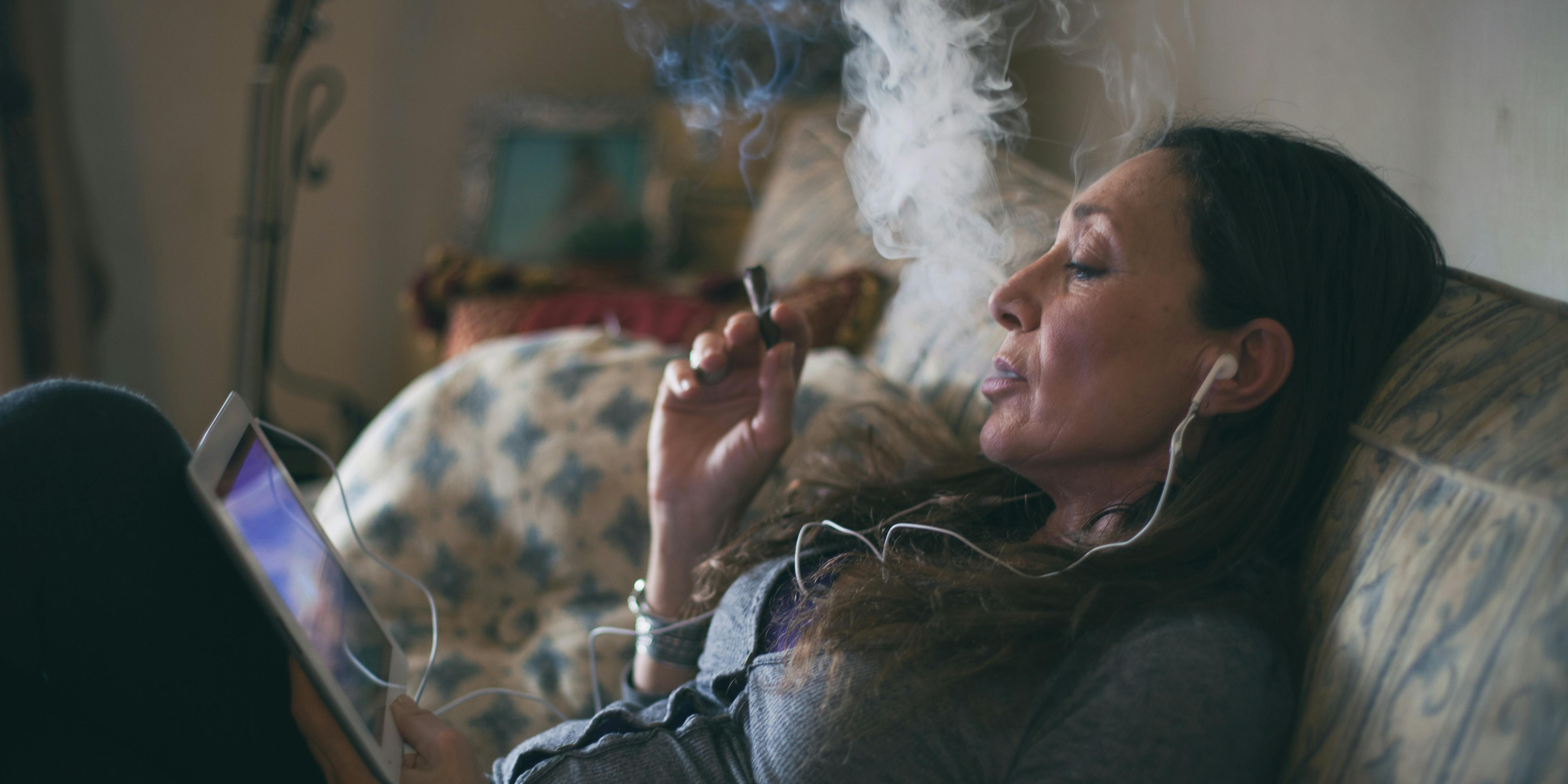 Woman relaxing on a couch, smoking a cigar and watching a video on a tablet. These are essentials for parents who smoke weed.