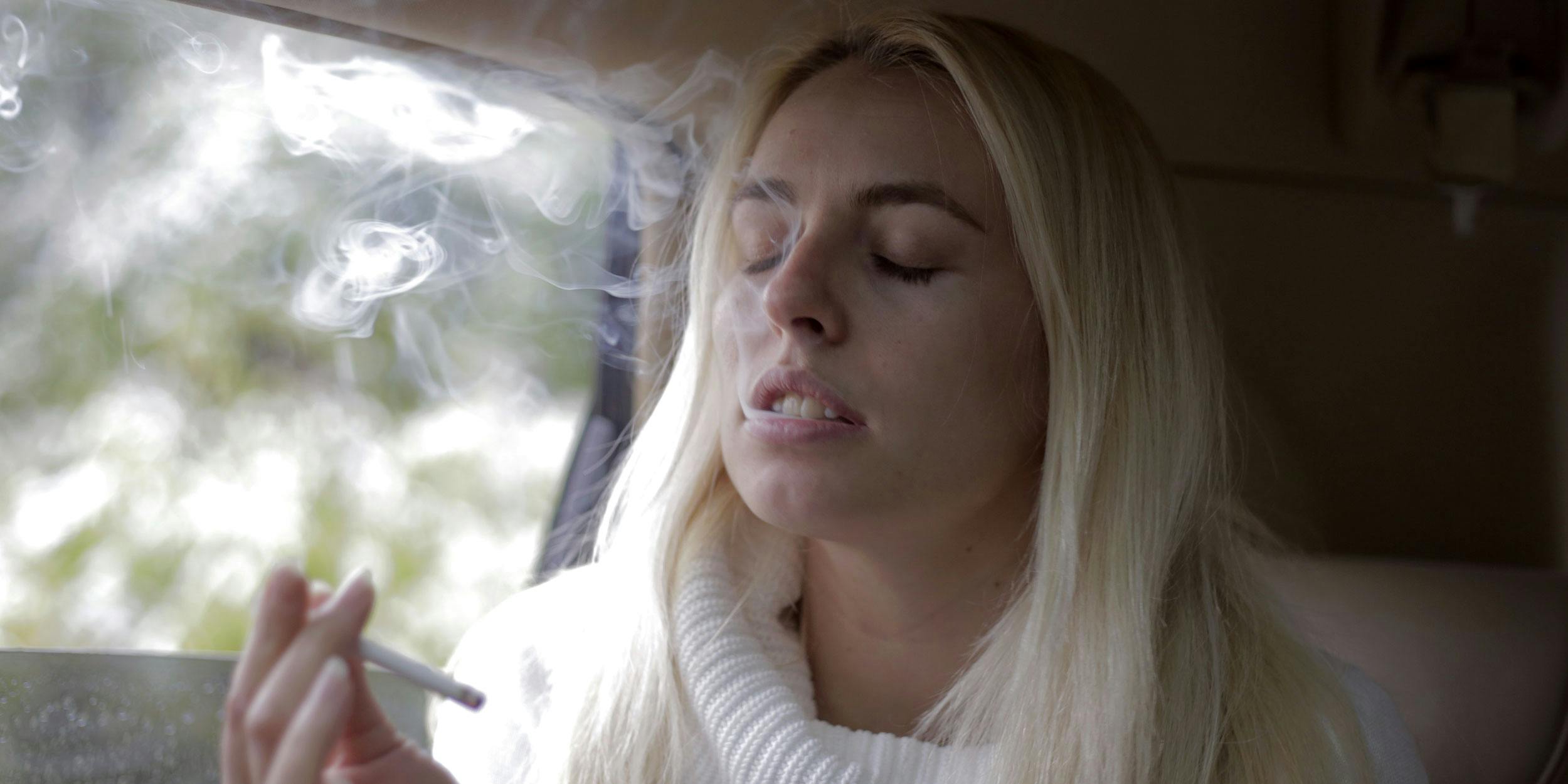 California is paying people to drive high for science. Here, a woman is shown in a car with a joint