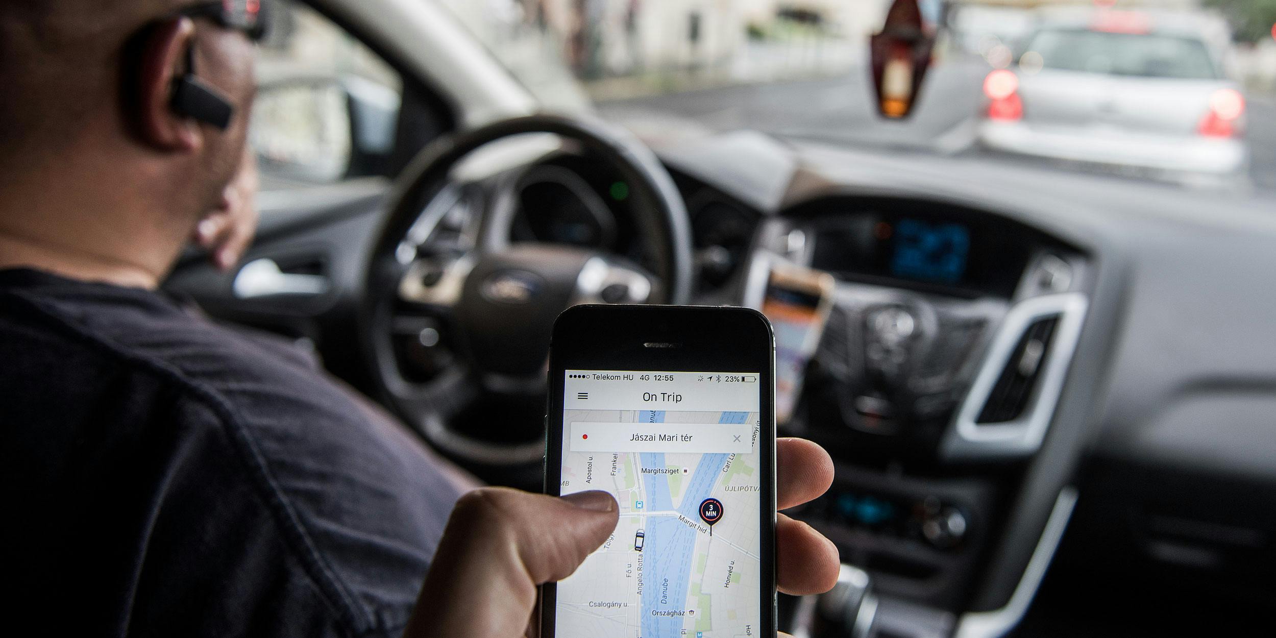 A passenger holds an iPhone displaying the Uber Technologies Inc. car service taxi application.