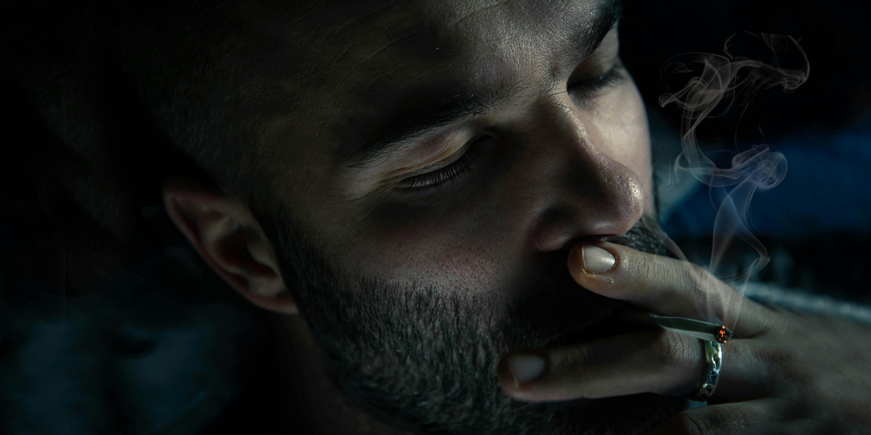 Close-up photo of mid-adult man smoking cigarette in the dark. He appears deep in thought, likely pondering one of life's many philosophical questions.