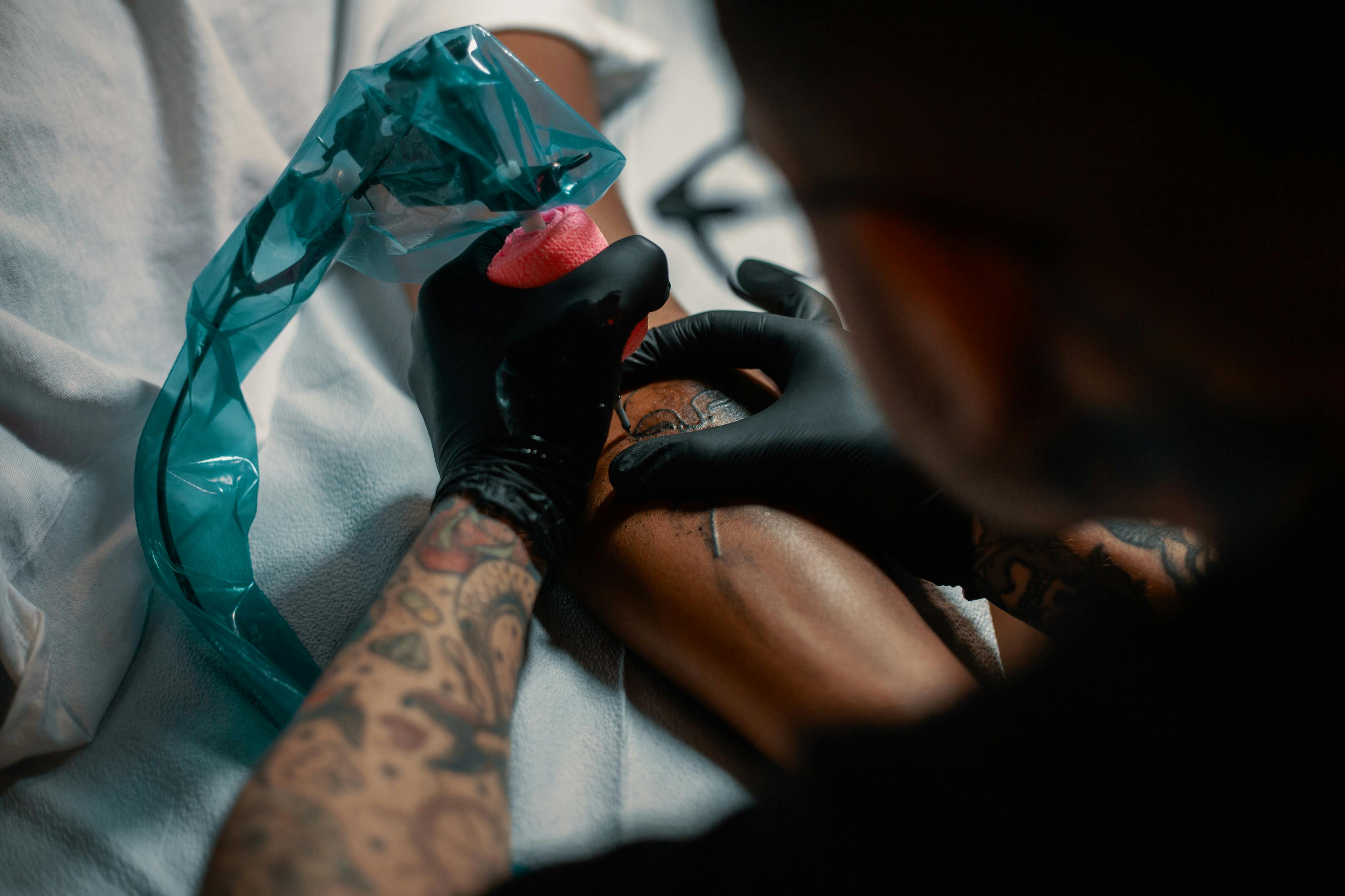 Smoking Weed Before a Tattoo: A tattoo artist with gloved hands operating a machine on a mans arm.