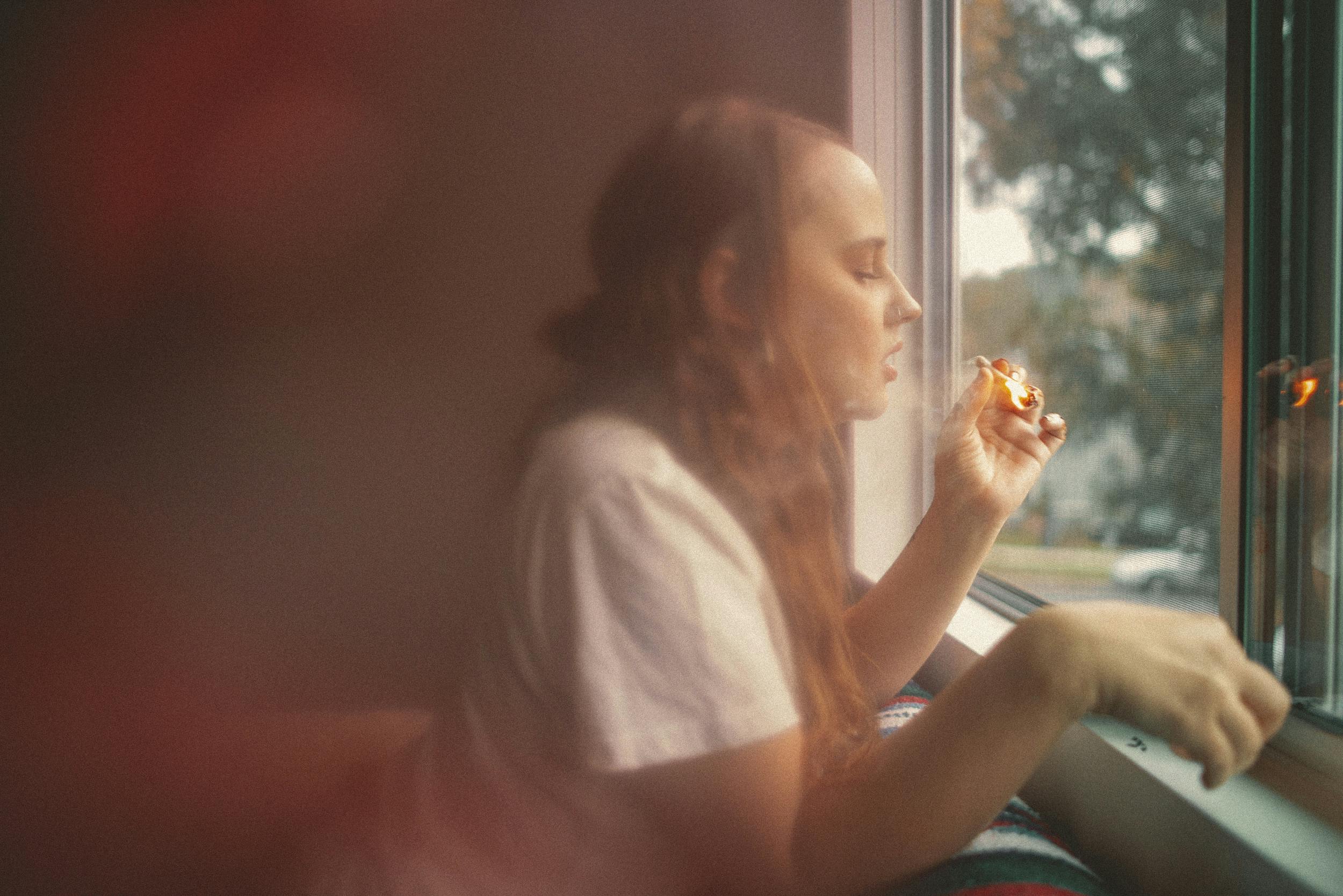 A woman leans out of a window smoking one of the best weed strains