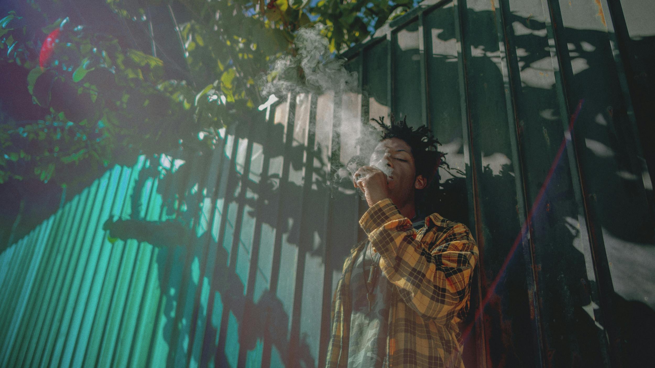 A man leans against a fence and enjoys one of the best weed vaporizers