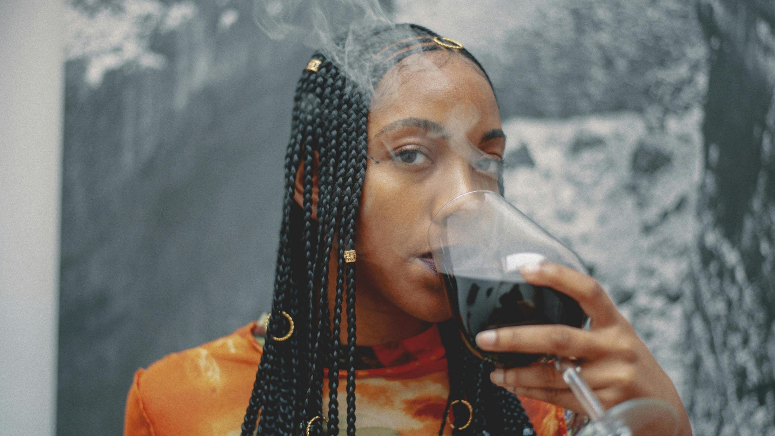 A woman takes a sip of weed wine in a cloud of smoke