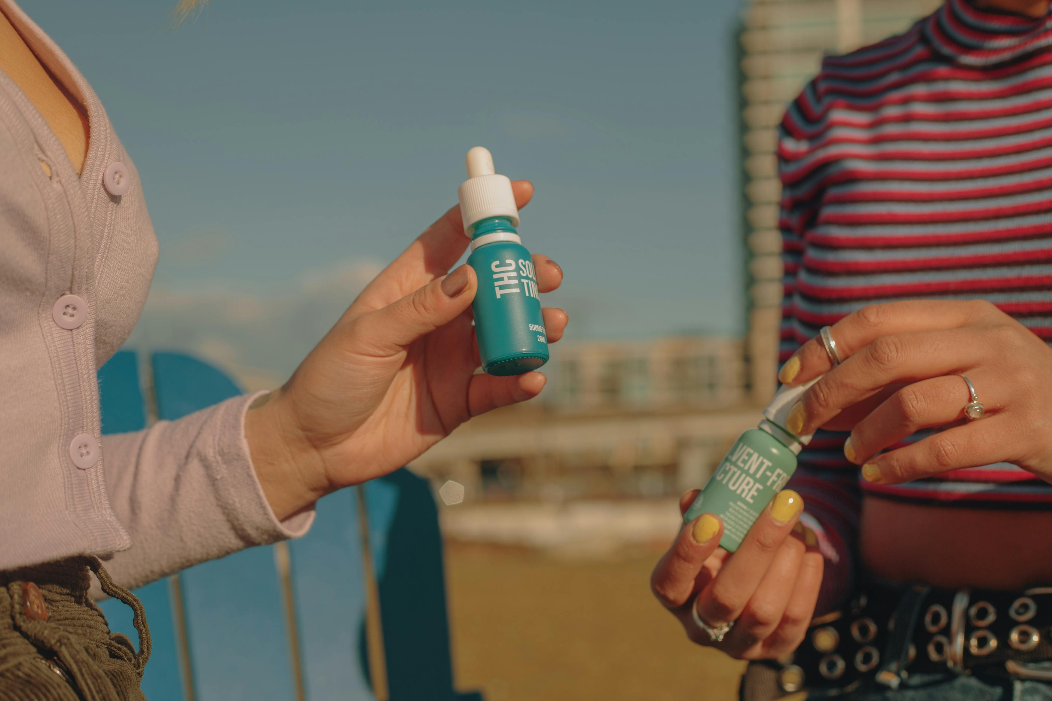 Two women hold two bottles of cannabis tinctures.