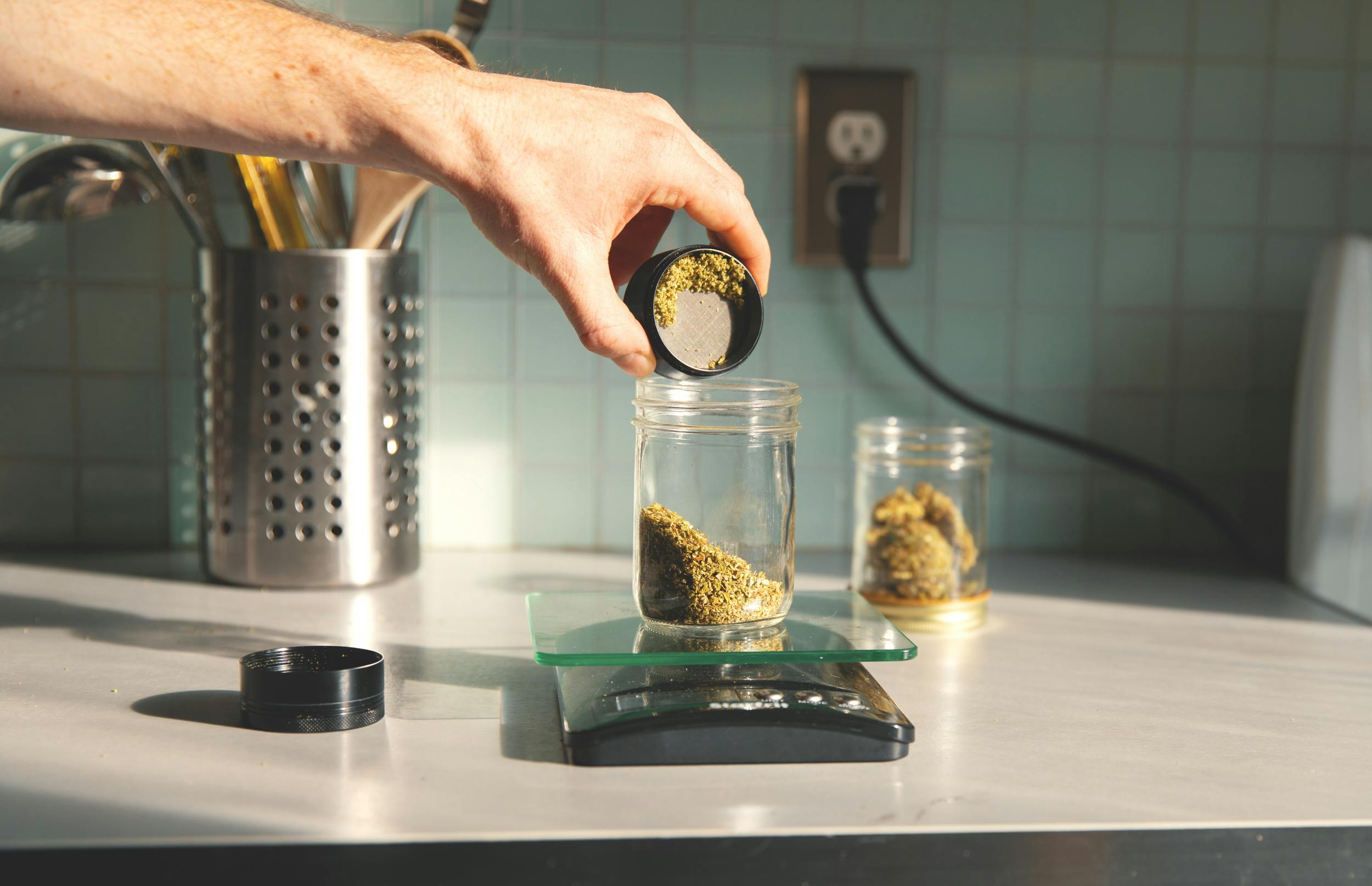 A hand pours ground flower into a jar as part of our how to make THC pills guide