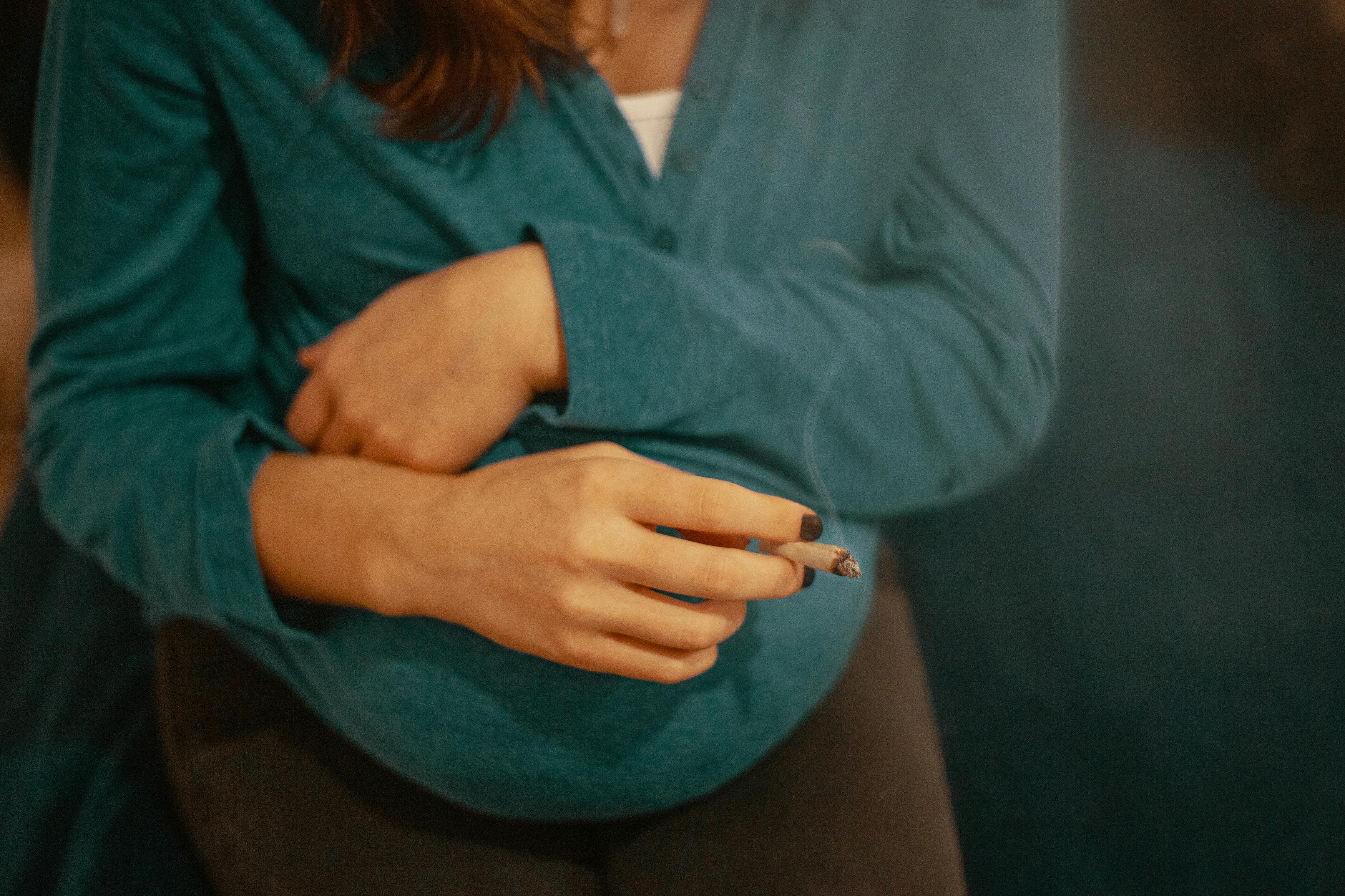 A woman holds a joint while crossing her hands over her pregnant stomach. Here's what you need to know about smoking weed during pregnancy