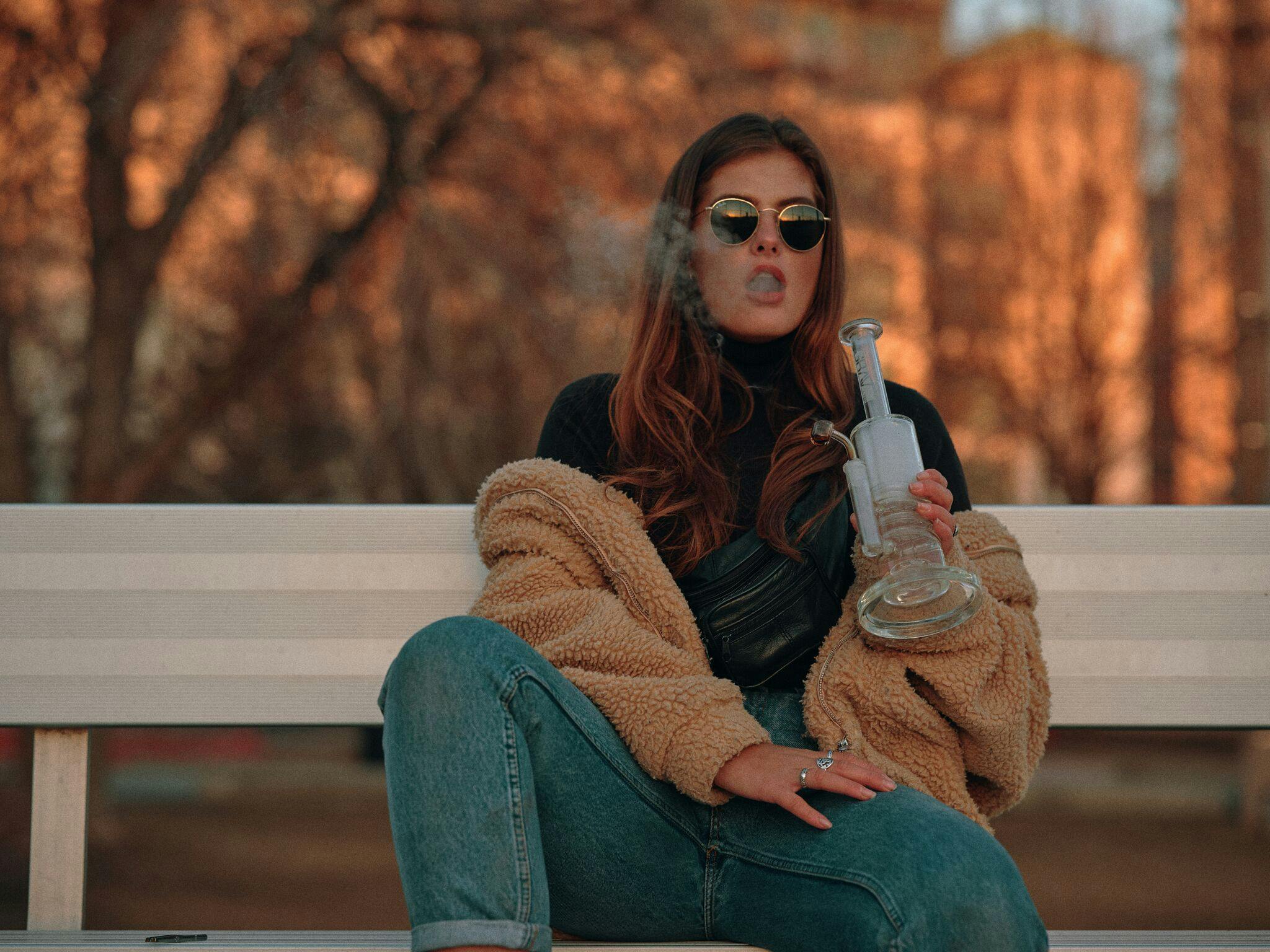 A woman holds a dab rig as she smokes rosin which she just made at home
